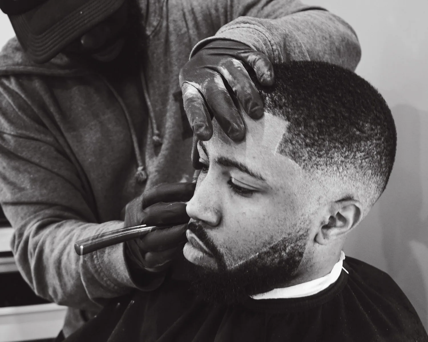 Barber shaping a client's beard line-up with a straight razor at Trims in Thornton Heath